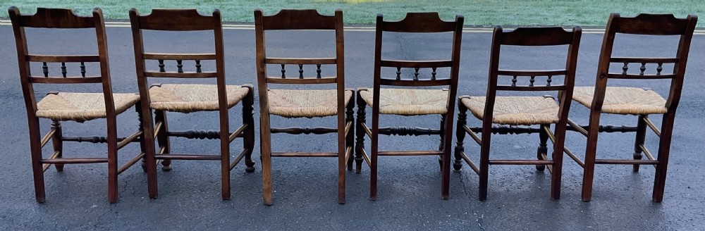 A set of six dark wooden elm dining chairs featuring hand-woven rush seats, turned front stretchers, and spindle back detail. View VIII