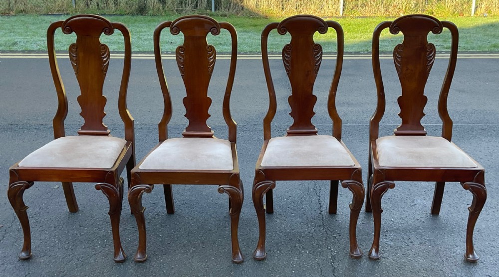 A set of four mahogany highback dining chairs featuring carved vase-shaped back splats, cabriole front legs, and neutral fabric upholstered seats.