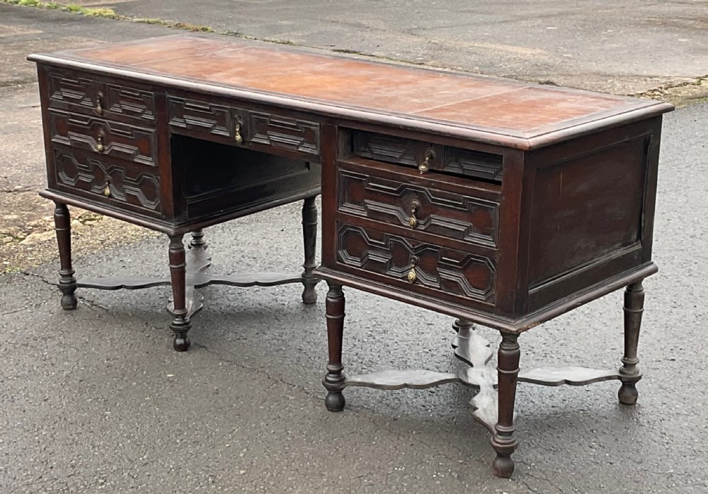 A large dark oak pedestal writing desk featuring geometric panelled drawer fronts, a leather inset writing surface, turned legs, and cross stretchers. View II