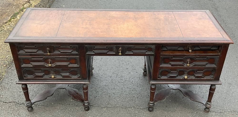 A large dark oak pedestal writing desk featuring geometric panelled drawer fronts, a leather inset writing surface, turned legs, and cross stretchers. View III