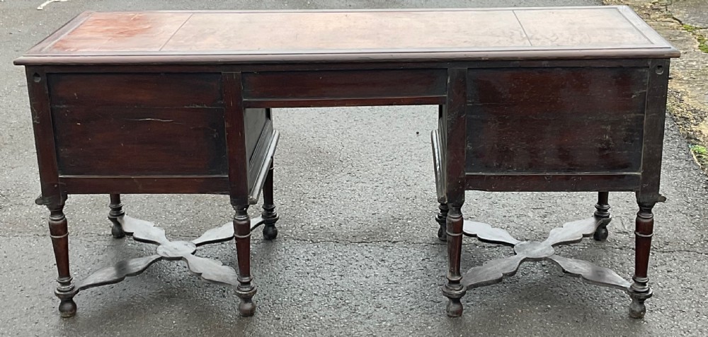 A large dark oak pedestal writing desk featuring geometric panelled drawer fronts, a leather inset writing surface, turned legs, and cross stretchers. View IV