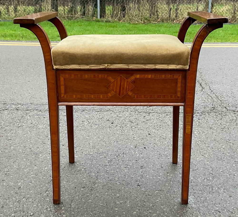 An Edwardian mahogany piano stool with curved side handles, green velvet upholstered seat, and geometric wood inlay on the apron.