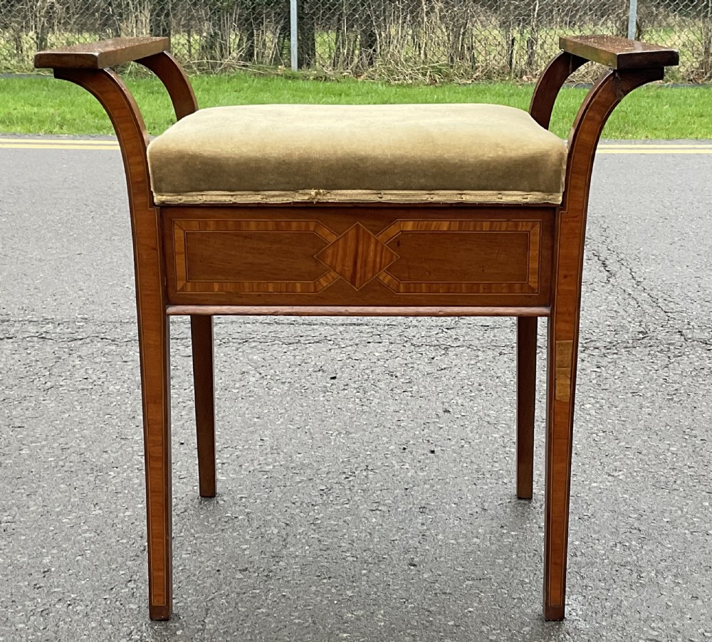 An Edwardian mahogany piano stool with curved side handles, green velvet upholstered seat, and geometric wood inlay on the apron. View II