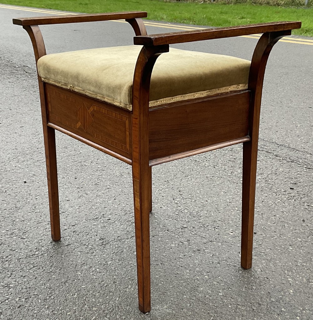 An Edwardian mahogany piano stool with curved side handles, green velvet upholstered seat, and geometric wood inlay on the apron. View VI