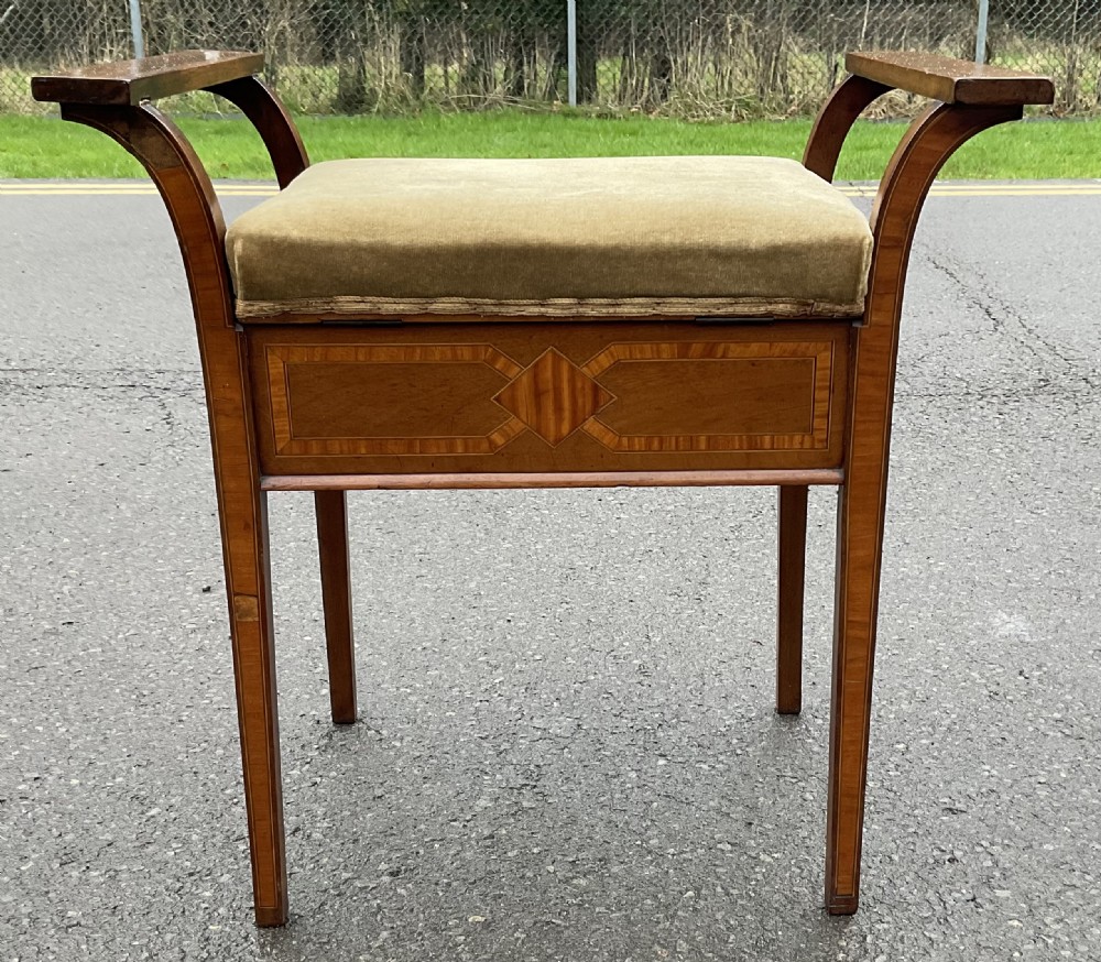 An Edwardian mahogany piano stool with curved side handles, green velvet upholstered seat, and geometric wood inlay on the apron. View X