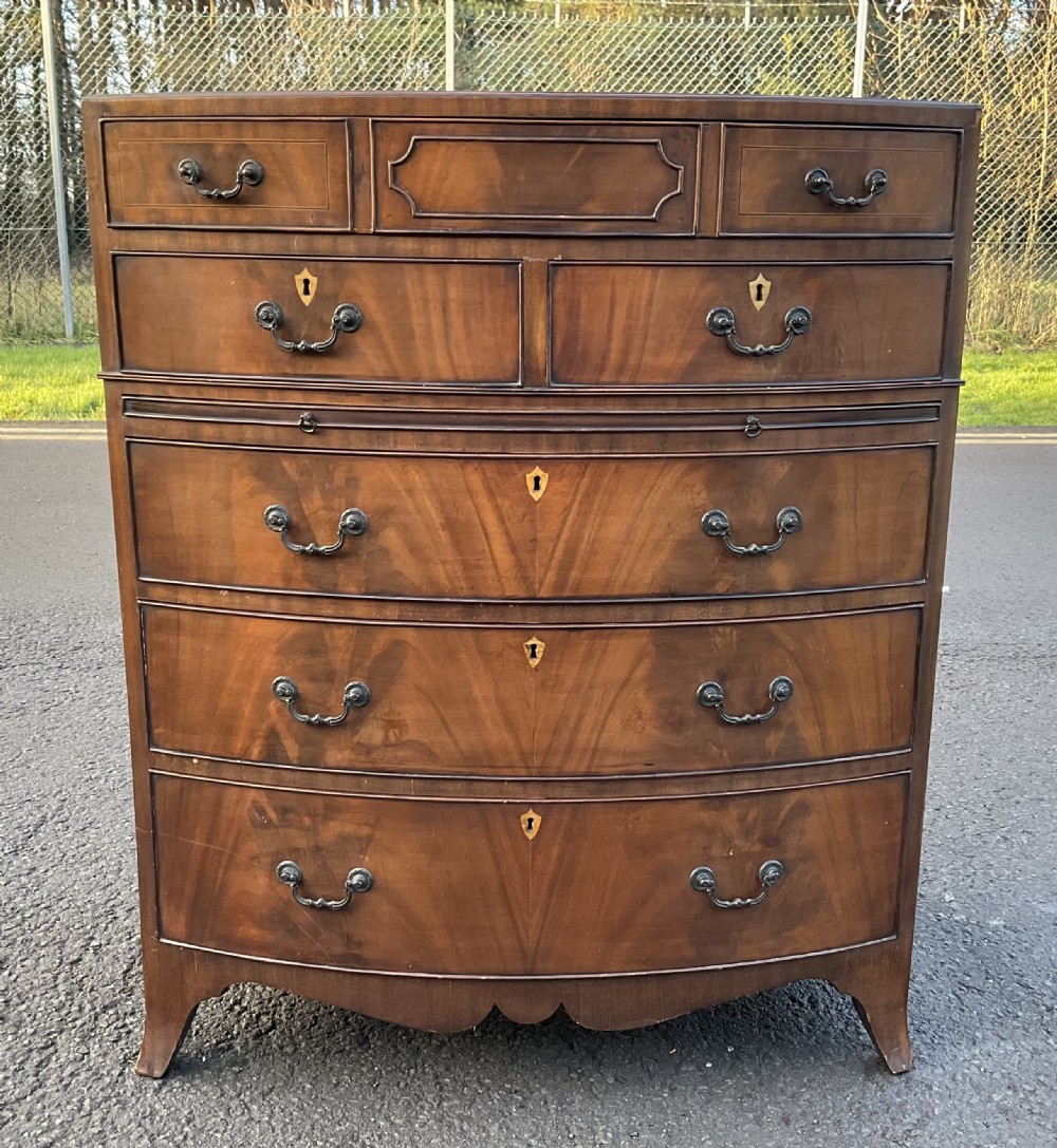 A Georgian style mahogany bowfront chest of drawers featuring brass handles, keyhole escutcheons, subtle string inlay, and splayed bracket feet. View II