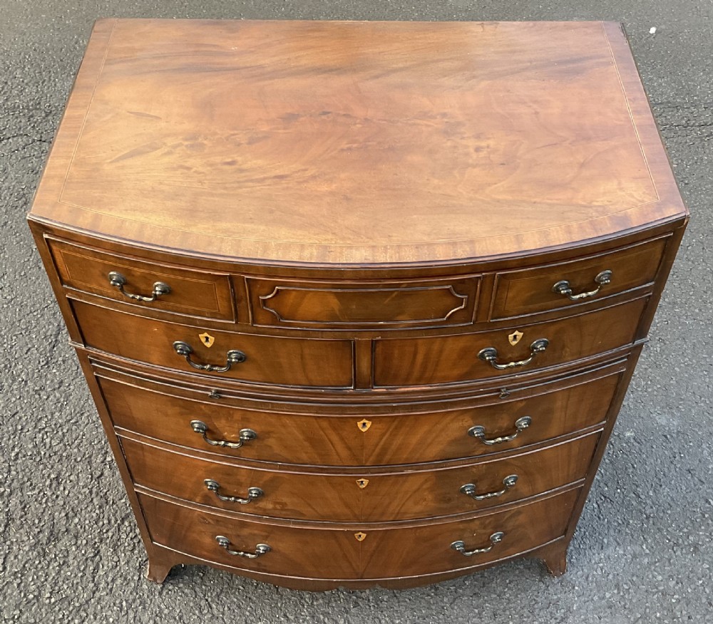 A Georgian style mahogany bowfront chest of drawers featuring brass handles, keyhole escutcheons, subtle string inlay, and splayed bracket feet. View III