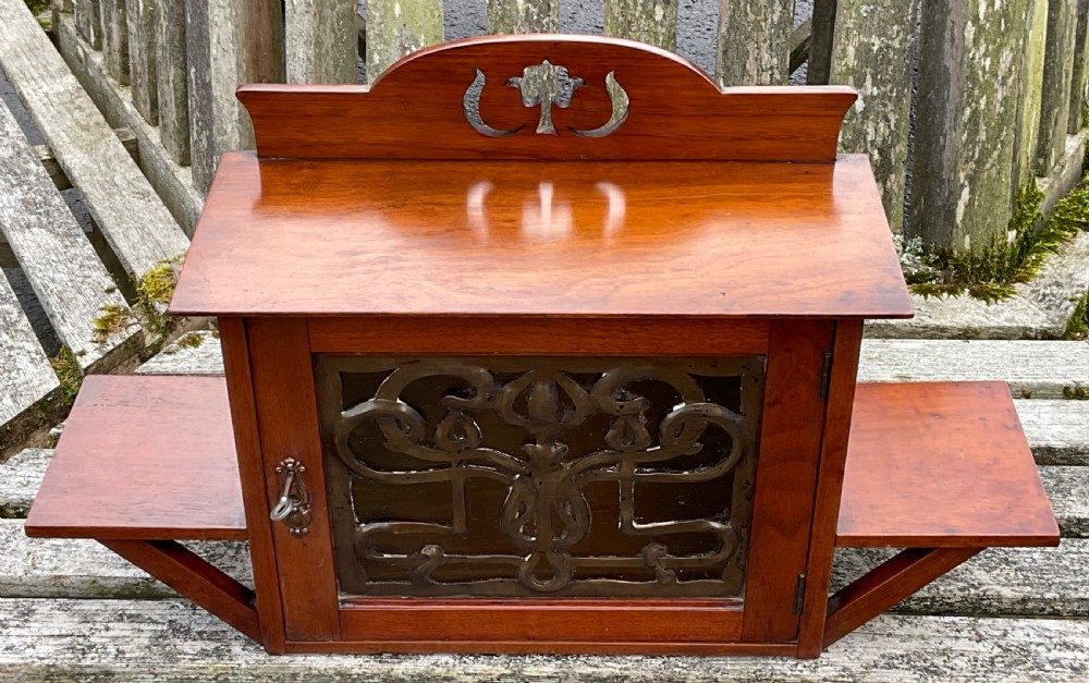 An Art Nouveau mahogany hanging wall cabinet featuring a central door with a decorative copper panel flanked by two side display shelves and topped with a pierced pediment. View III