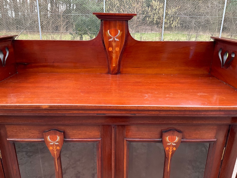 An Art Nouveau mahogany glazed bookcase featuring two glass panel doors with stylised botanical wood inlay and a raised gallery top. View XI