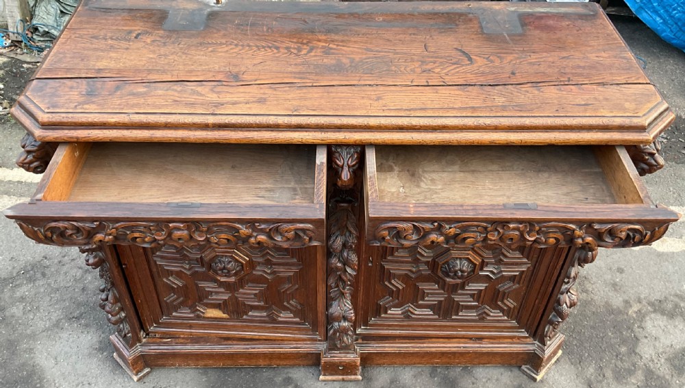 A dark Victorian carved oak sideboard featuring an ornate scrollwork cresting, tiered upper shelves, carved lion masks, and geometric panelled doors. View IV