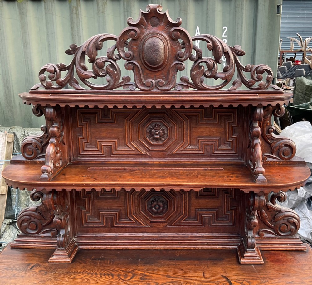 A dark Victorian carved oak sideboard featuring an ornate scrollwork cresting, tiered upper shelves, carved lion masks, and geometric panelled doors. View VII