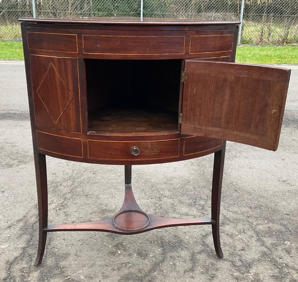 A Georgian mahogany standing corner cupboard featuring a bowfront cabinet, oval inlaid panel, single lower drawer, and curved legs connected by a shaped stretcher. View IX