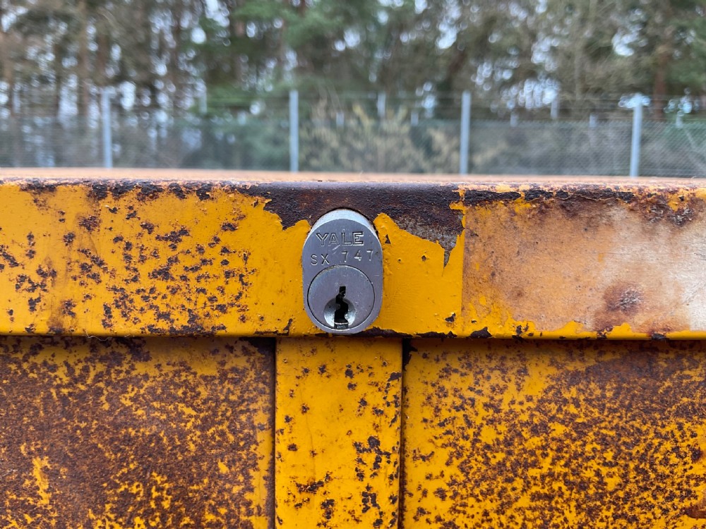 A tall industrial yellow steel cabinet featuring fourteen small drawers with integrated metal handles and label frames, displaying a weathered patina. View X