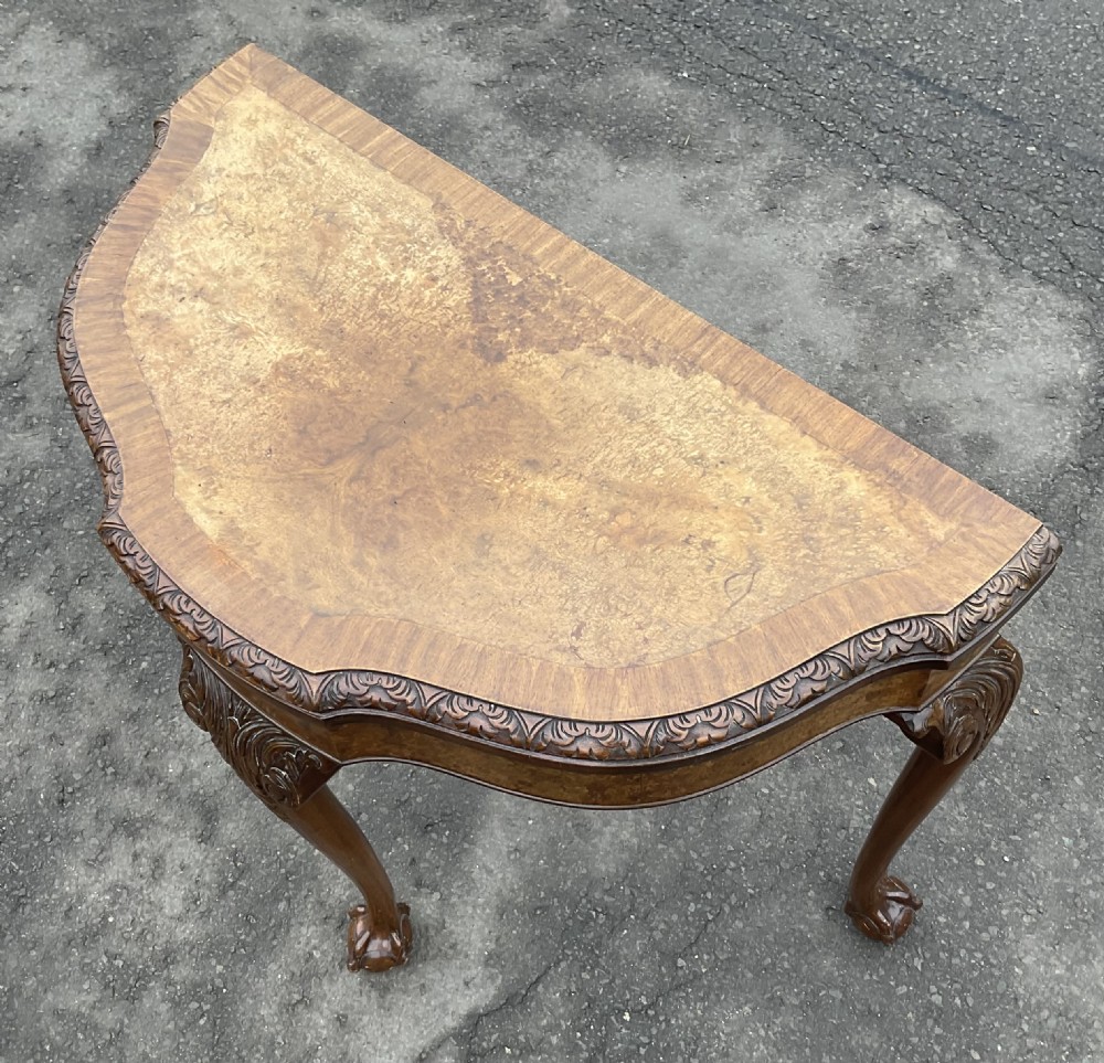 A semi-circular Queen Anne style burr walnut card table featuring a fold-over top, carved foliate border, and cabriole legs with ball-and-claw feet. View VII