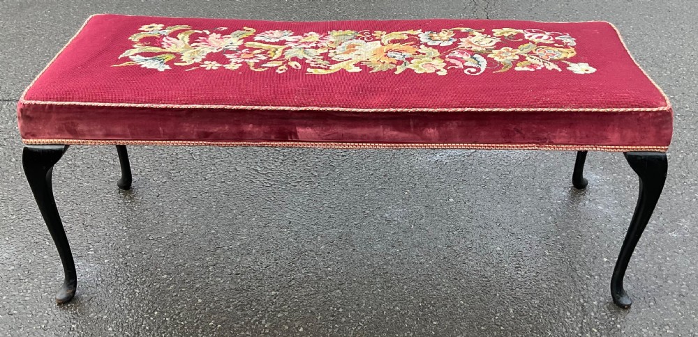 A long rectangular upholstered dressing stool featuring a deep red wool needlepoint top with central floral embroidery and ebonised cabriole legs.
