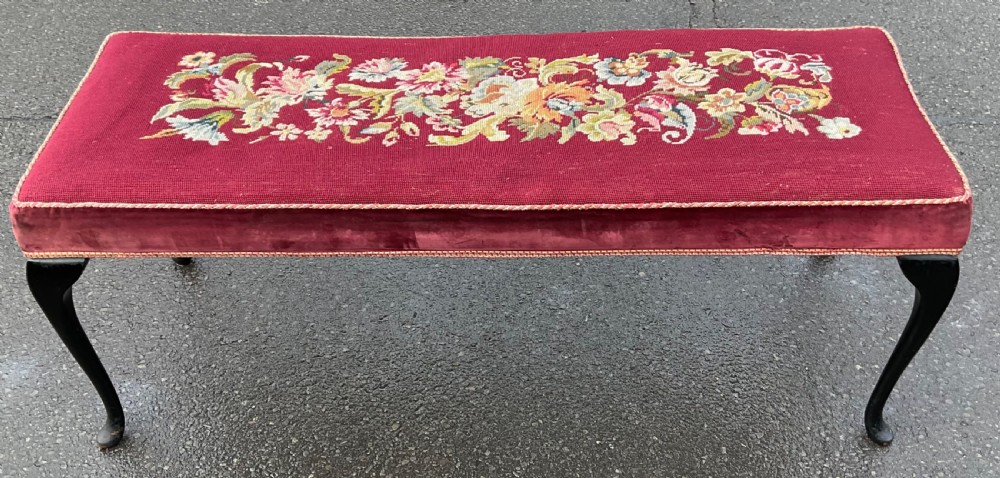 A long rectangular upholstered dressing stool featuring a deep red wool needlepoint top with central floral embroidery and ebonised cabriole legs. View II