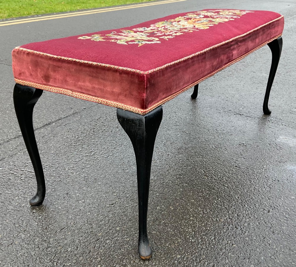 A long rectangular upholstered dressing stool featuring a deep red wool needlepoint top with central floral embroidery and ebonised cabriole legs. View IV