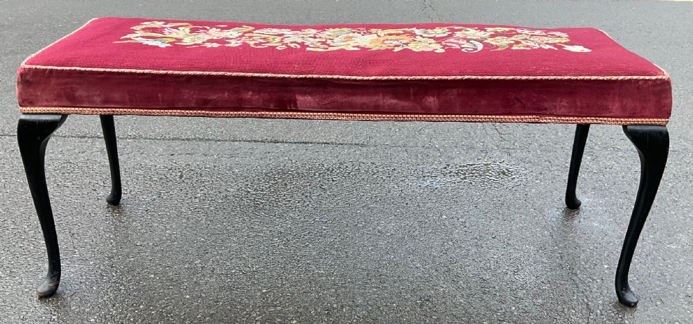 A long rectangular upholstered dressing stool featuring a deep red wool needlepoint top with central floral embroidery and ebonised cabriole legs. View V