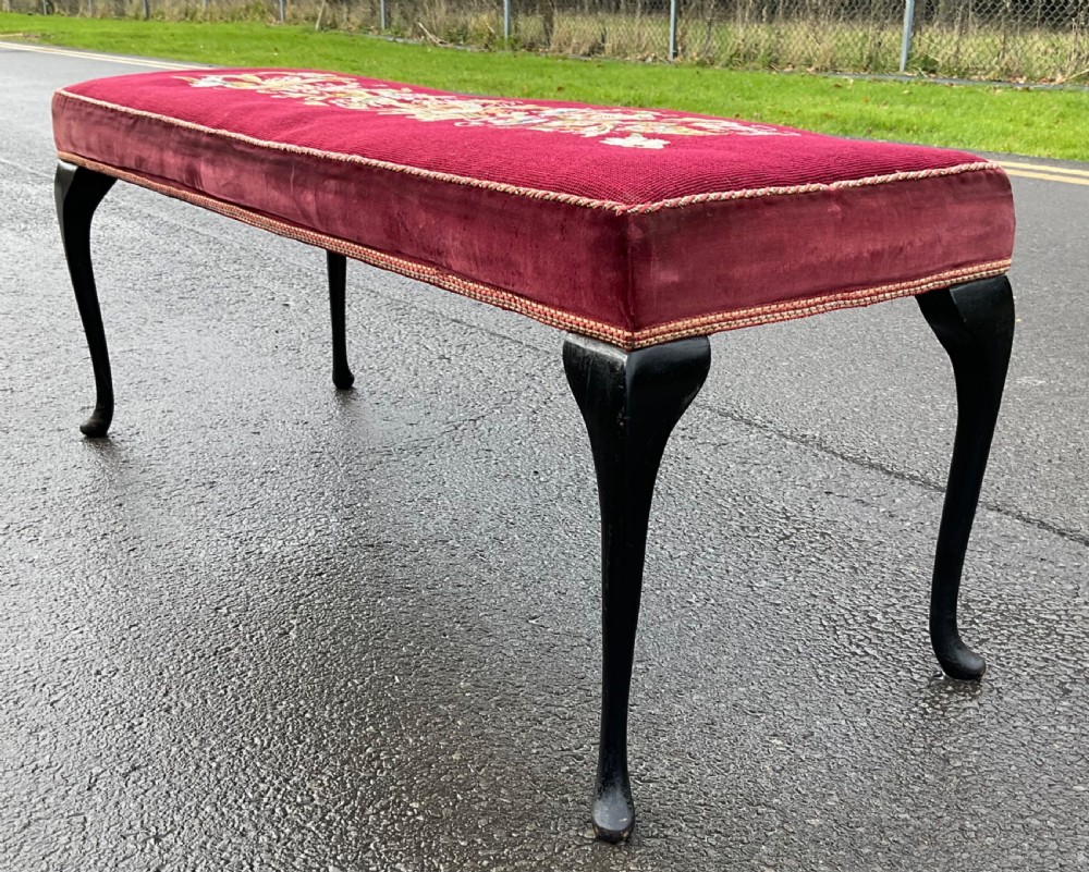 A long rectangular upholstered dressing stool featuring a deep red wool needlepoint top with central floral embroidery and ebonised cabriole legs. View VI