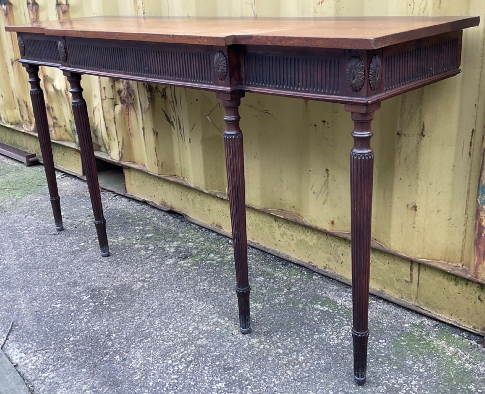 A Georgian style mahogany breakfront console table featuring a projecting centre top, fluted frieze, carved rosette corner medallions, and four tapered reeded legs. View V