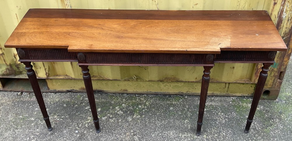 A Georgian style mahogany breakfront console table featuring a projecting centre top, fluted frieze, carved rosette corner medallions, and four tapered reeded legs. View VI