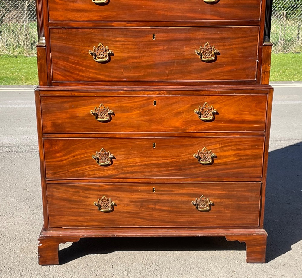 A tall Georgian flame mahogany chest on chest featuring brass bail handles, oval fan inlays along the top frieze, and bracket feet. View IV