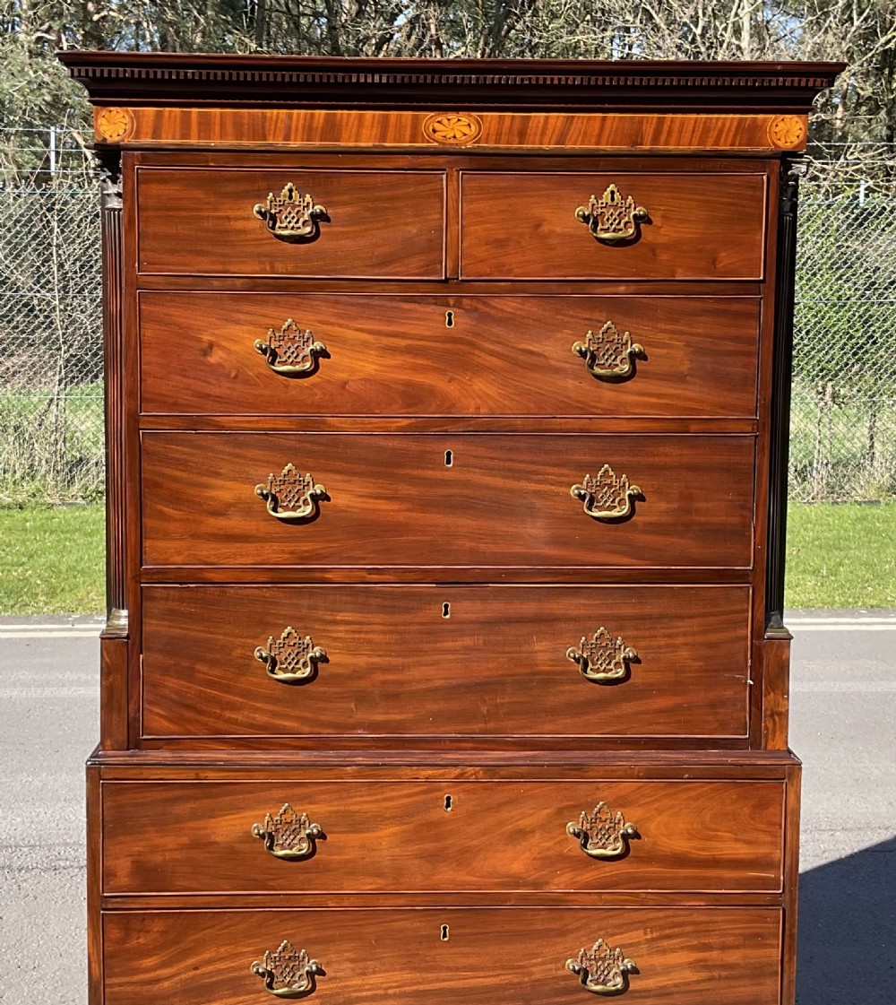 A tall Georgian flame mahogany chest on chest featuring brass bail handles, oval fan inlays along the top frieze, and bracket feet. View V