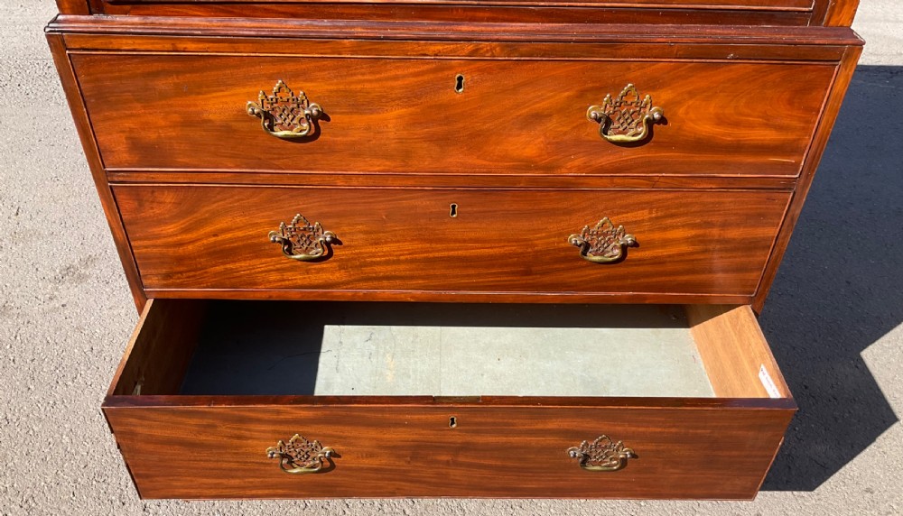 A tall Georgian flame mahogany chest on chest featuring brass bail handles, oval fan inlays along the top frieze, and bracket feet. View IX