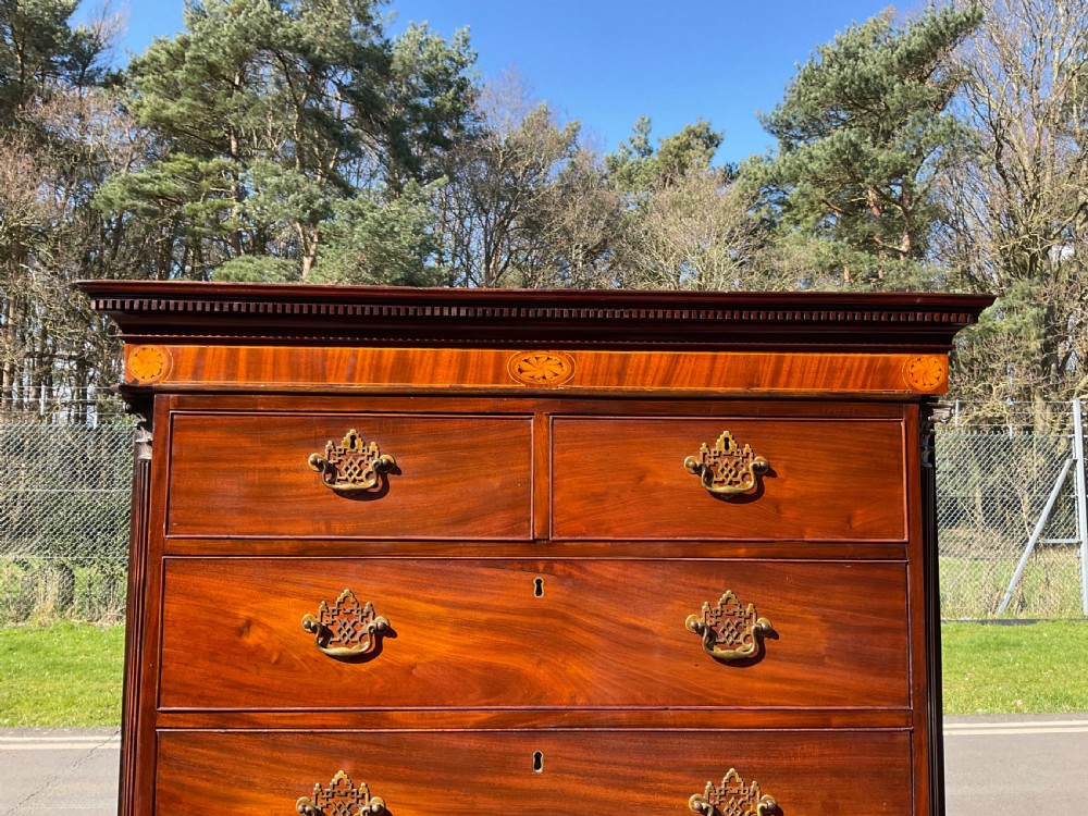 A tall Georgian flame mahogany chest on chest featuring brass bail handles, oval fan inlays along the top frieze, and bracket feet. View X