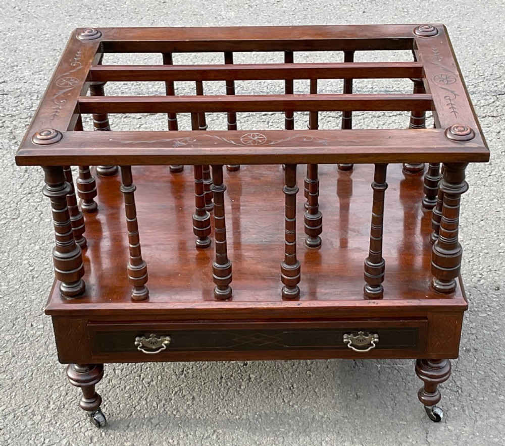 A Victorian dark mahogany Canterbury featuring vertical turned spindles, an inlaid top frame, a lower drawer with brass handles, and brass castors.