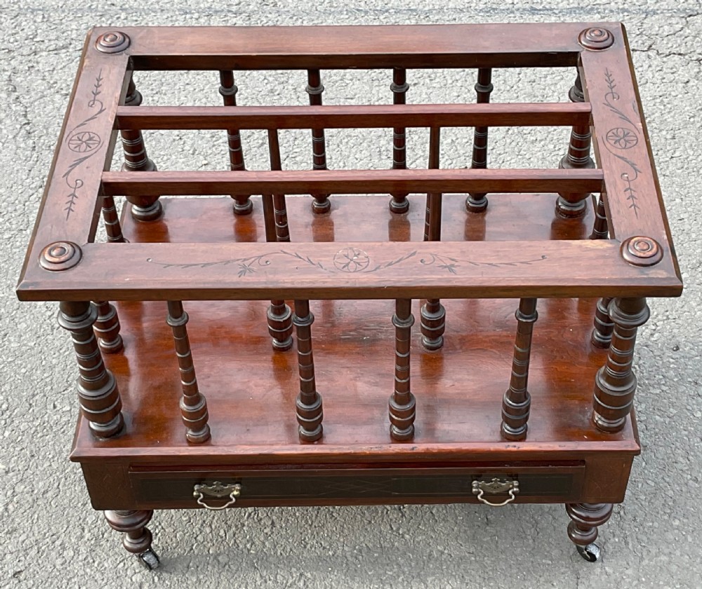 A Victorian dark mahogany Canterbury featuring vertical turned spindles, an inlaid top frame, a lower drawer with brass handles, and brass castors. View II