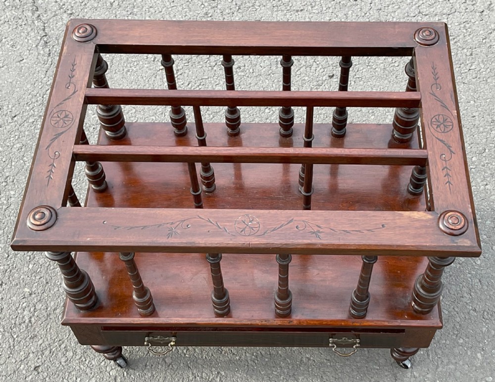 A Victorian dark mahogany Canterbury featuring vertical turned spindles, an inlaid top frame, a lower drawer with brass handles, and brass castors. View III