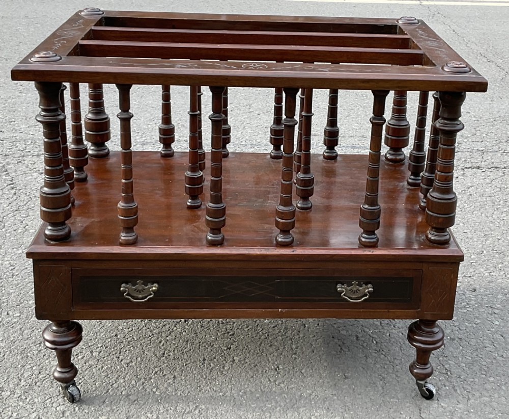 A Victorian dark mahogany Canterbury featuring vertical turned spindles, an inlaid top frame, a lower drawer with brass handles, and brass castors. View IV