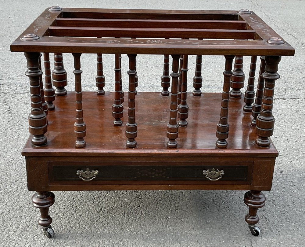A Victorian dark mahogany Canterbury featuring vertical turned spindles, an inlaid top frame, a lower drawer with brass handles, and brass castors. View VII