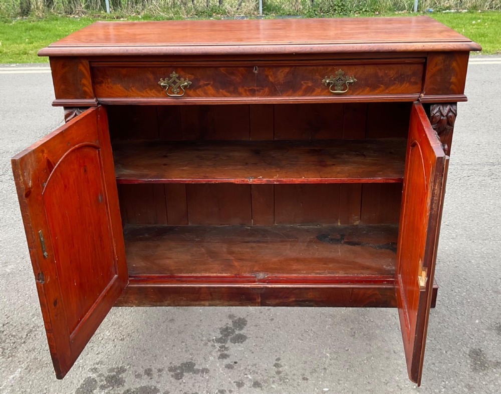 A Victorian mahogany two-door sideboard featuring flame mahogany door panels, carved scroll details, side corbels, and brass drawer handles. View VII