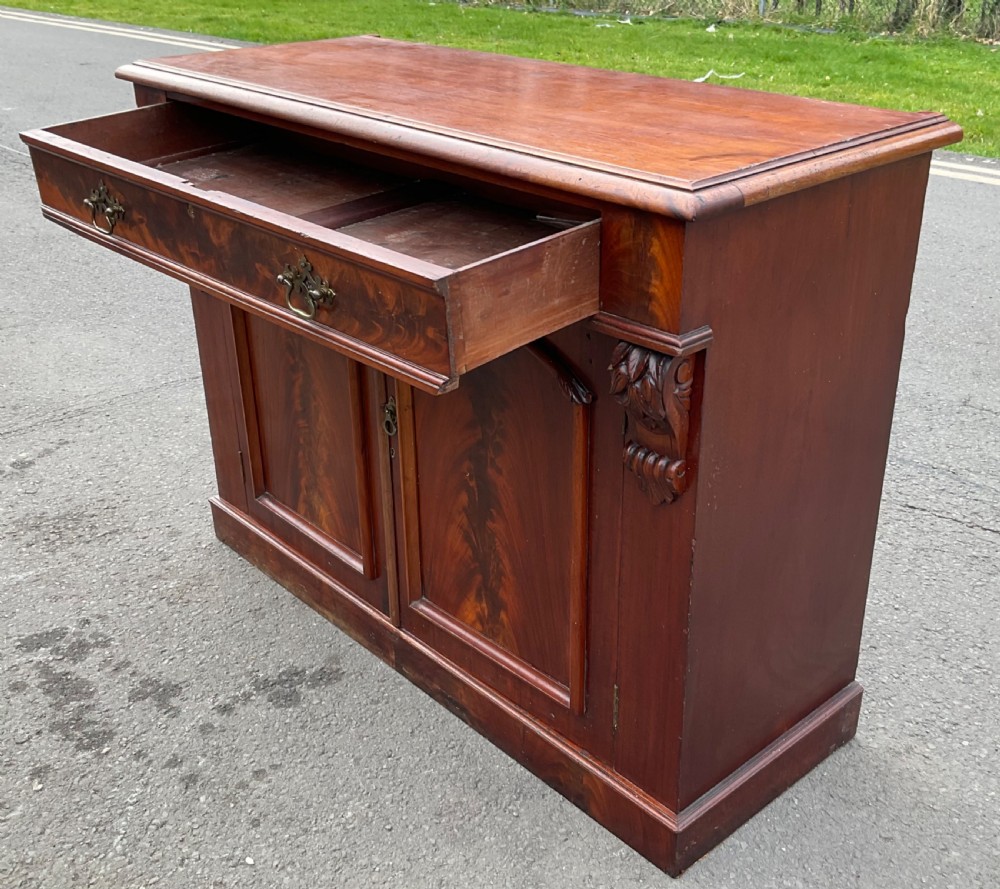 A Victorian mahogany two-door sideboard featuring flame mahogany door panels, carved scroll details, side corbels, and brass drawer handles. View VIII