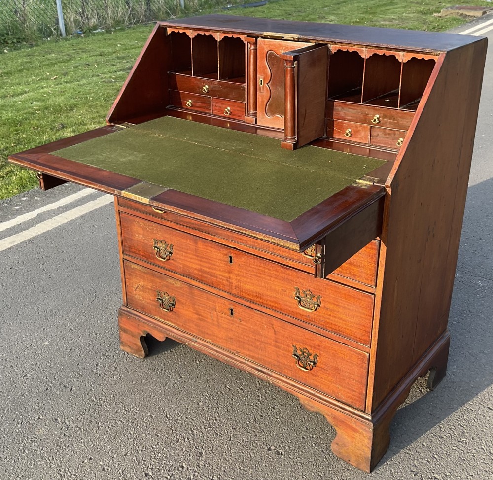 A Georgian mahogany slant-front writing bureau featuring four graduated drawers with pierced brass escutcheons and bracket feet. View X