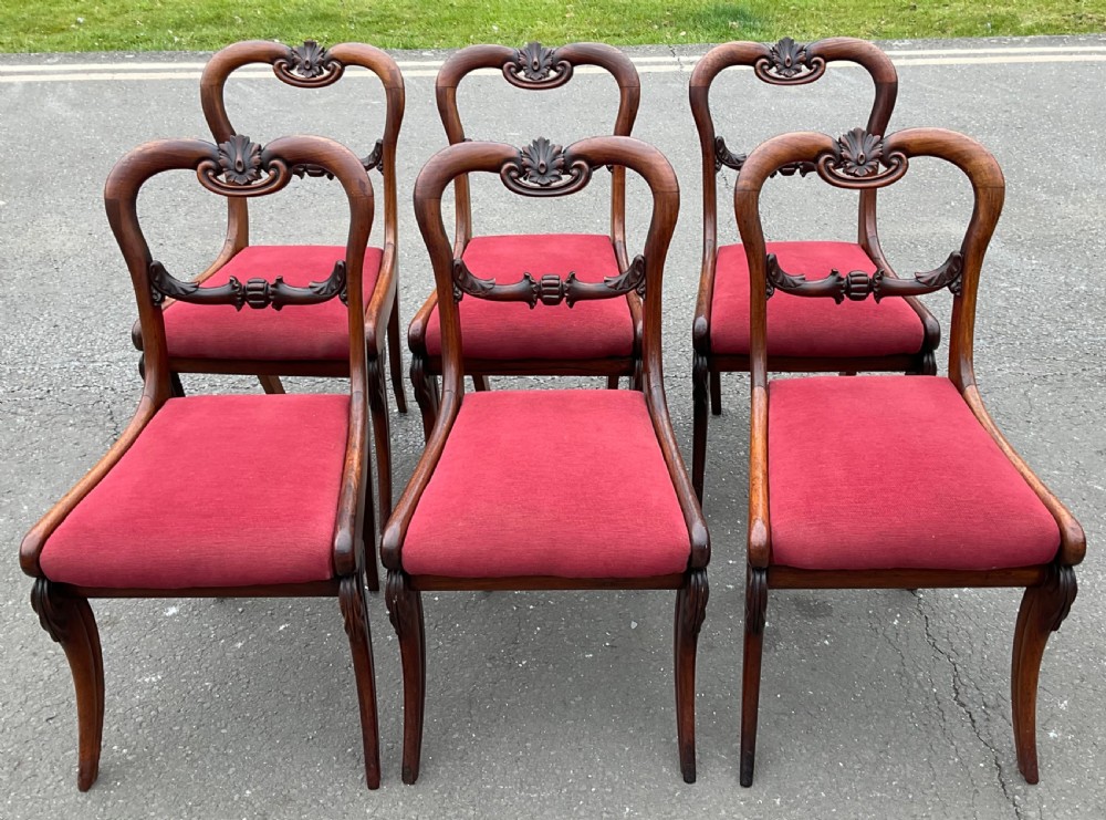 Set of six Regency rosewood dining chairs with carved balloon backs and red upholstered seats.