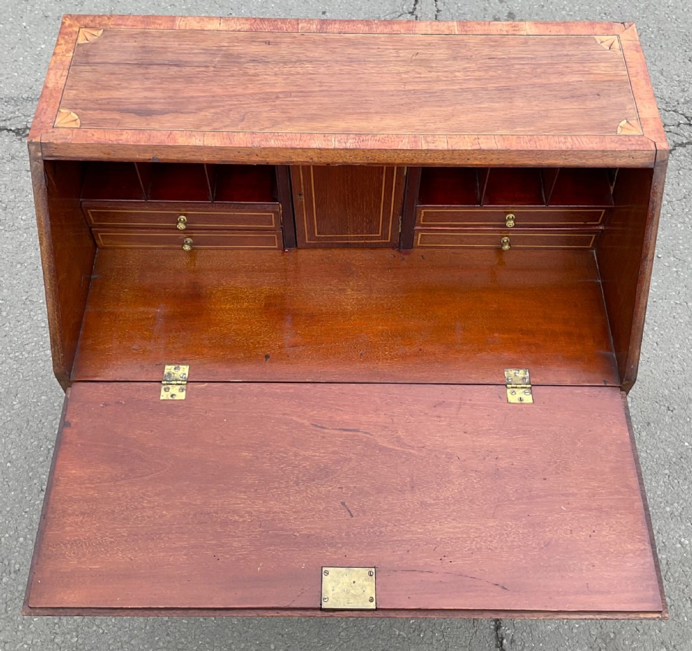 An Edwardian inlaid mahogany writing bureau featuring a sloped fall-front lid with a central oval marquetry motif above three drawers with brass handles. View VII