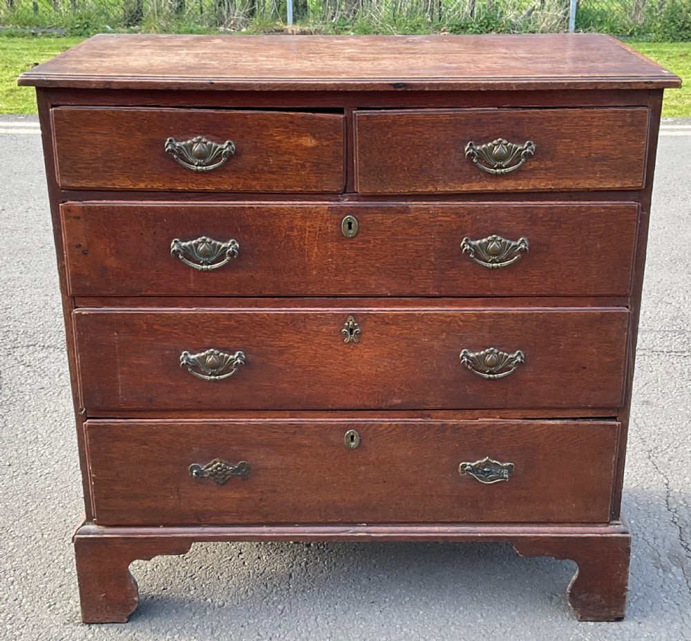 A Georgian oak chest of drawers featuring two short drawers over three long drawers with brass drop handles and bracket feet.