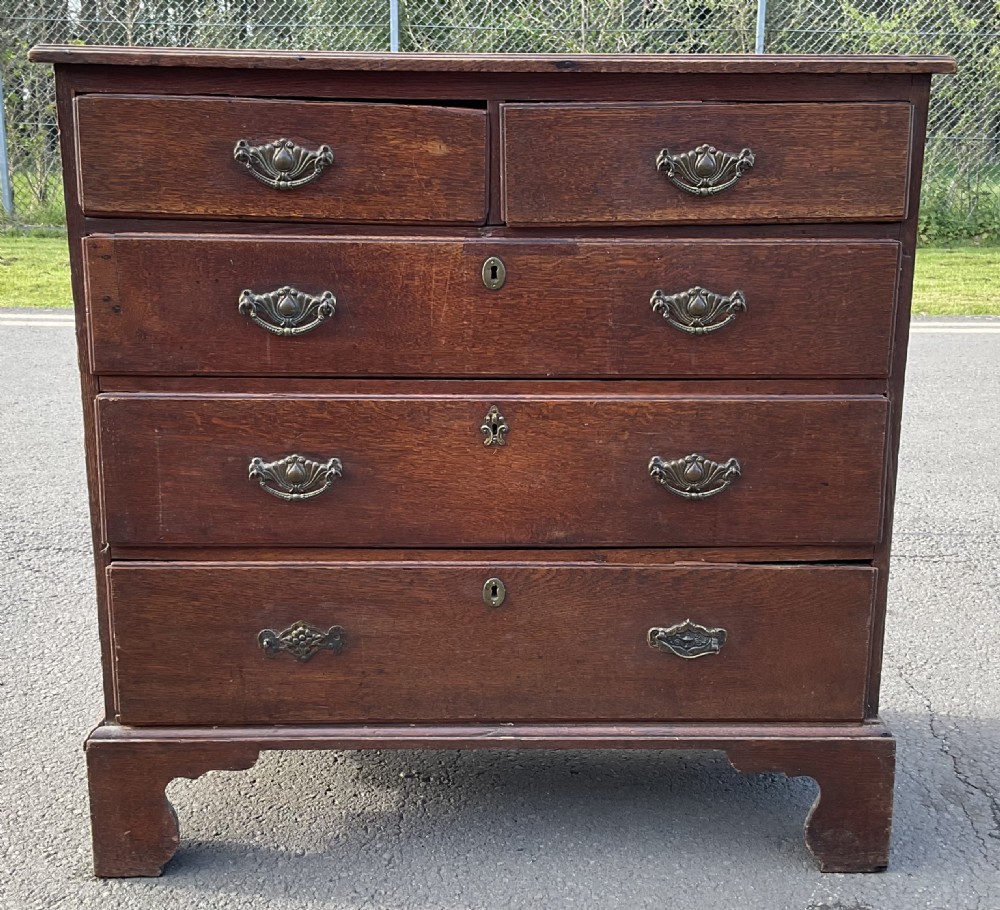 A Georgian oak chest of drawers featuring two short drawers over three long drawers with brass drop handles and bracket feet. View II