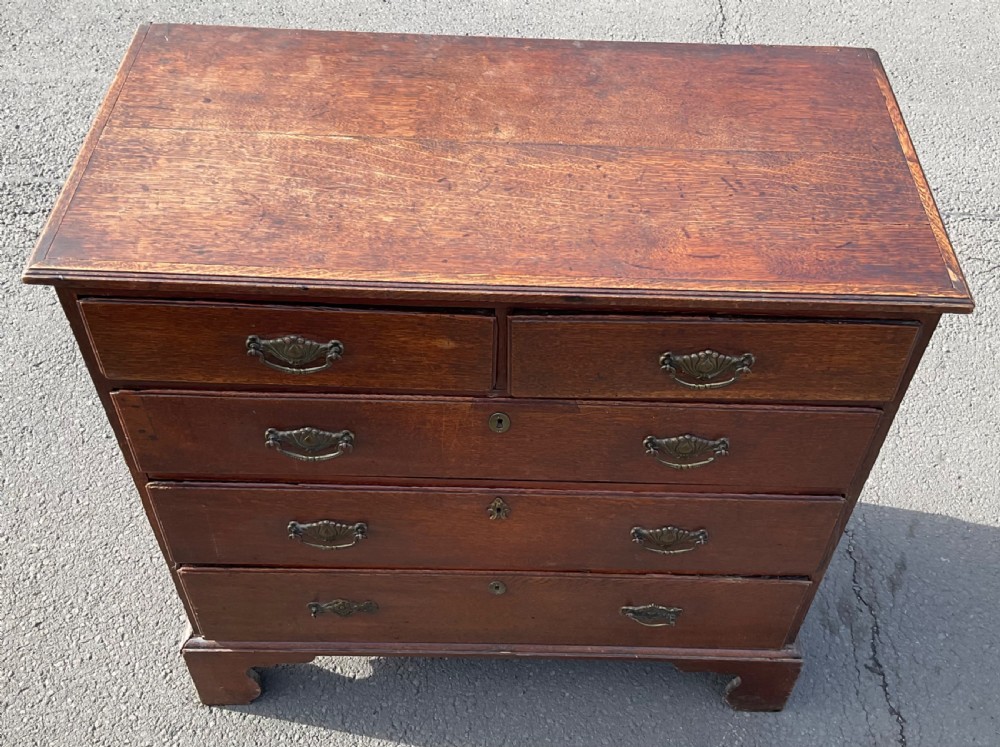A Georgian oak chest of drawers featuring two short drawers over three long drawers with brass drop handles and bracket feet. View VI