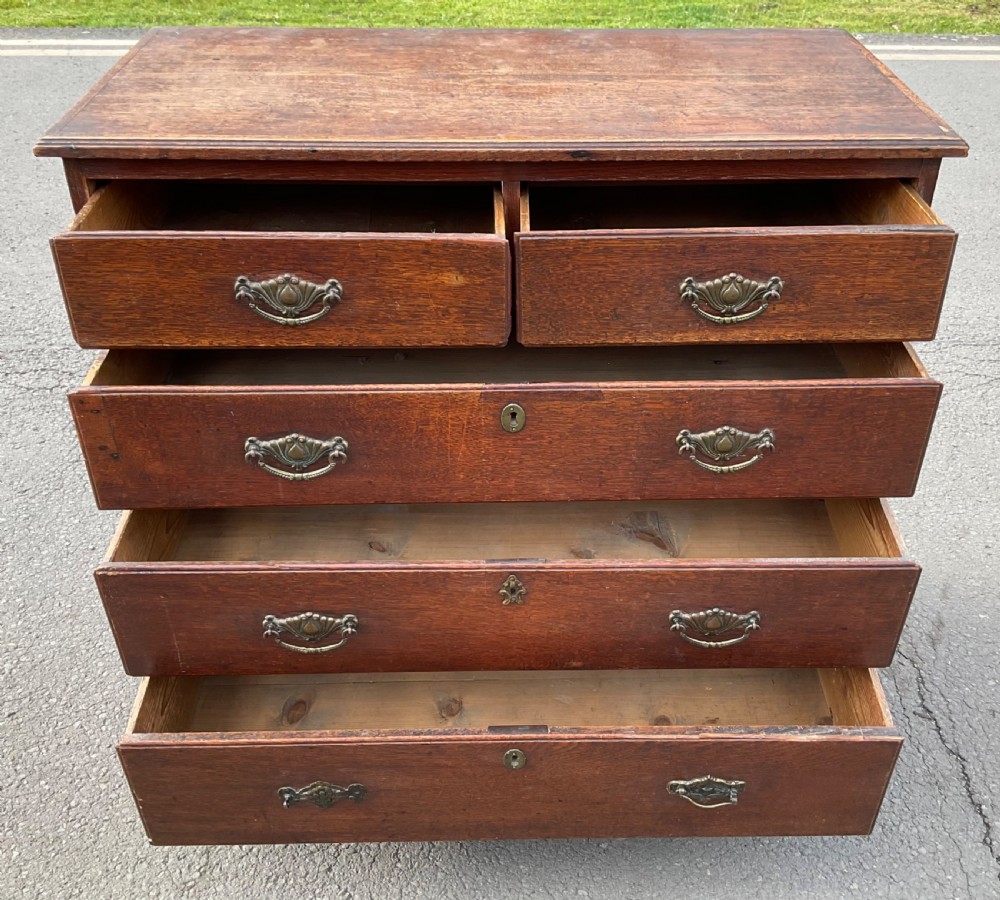 A Georgian oak chest of drawers featuring two short drawers over three long drawers with brass drop handles and bracket feet. View VII