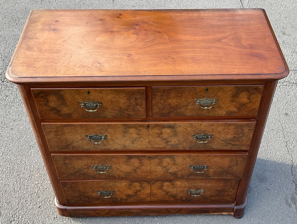 A Victorian burr walnut chest of drawers featuring a two-over-three drawer layout, decorative brass drop handles, and a solid plinth base. View III