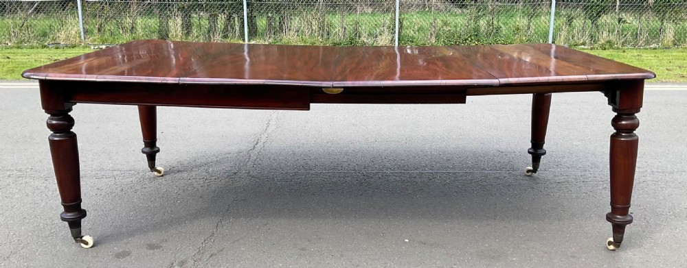 A large William IV mahogany extending dining table with turned tapered legs resting on brass and ceramic castors.