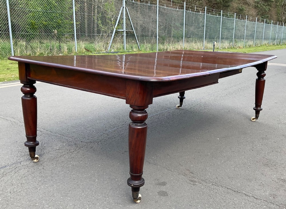 A large William IV mahogany extending dining table with turned tapered legs resting on brass and ceramic castors. View II