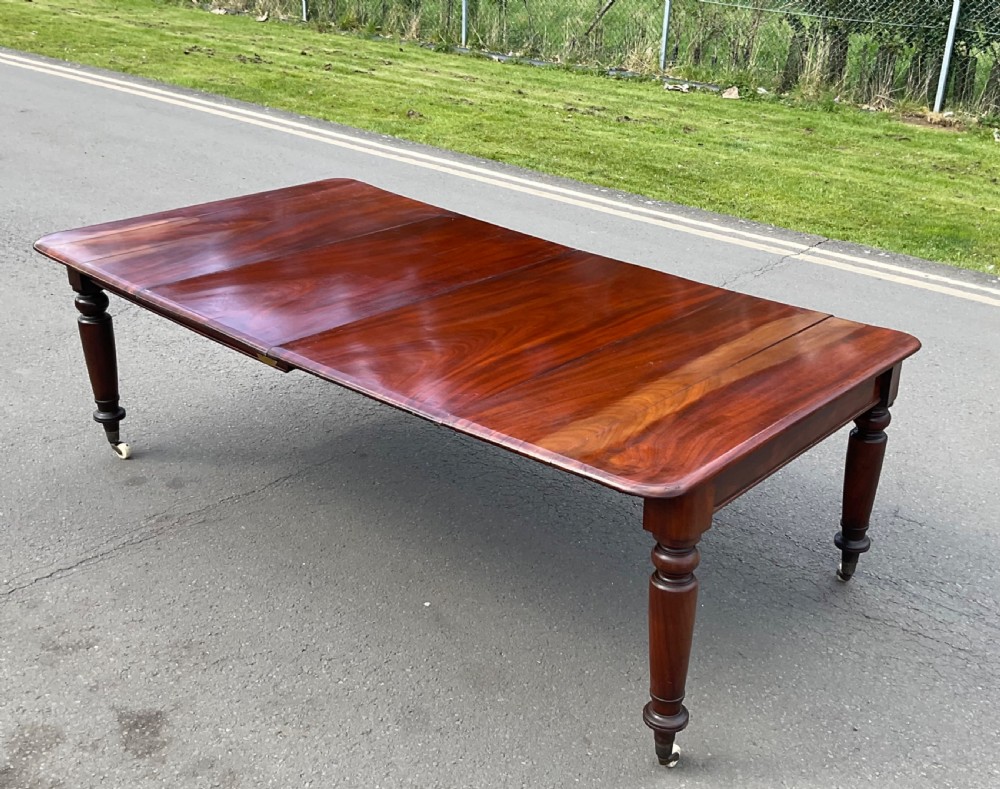 A large William IV mahogany extending dining table with turned tapered legs resting on brass and ceramic castors. View V