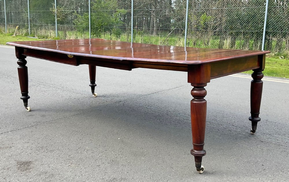 A large William IV mahogany extending dining table with turned tapered legs resting on brass and ceramic castors. View VI