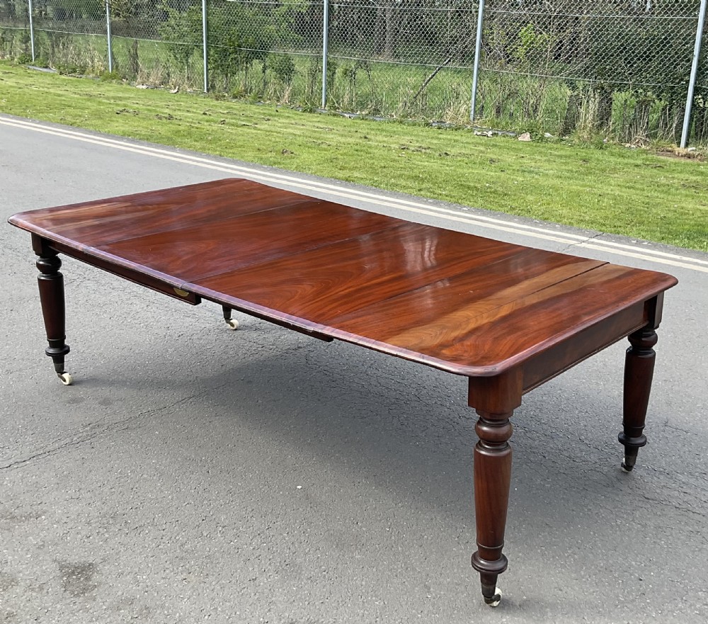 A large William IV mahogany extending dining table with turned tapered legs resting on brass and ceramic castors. View VII