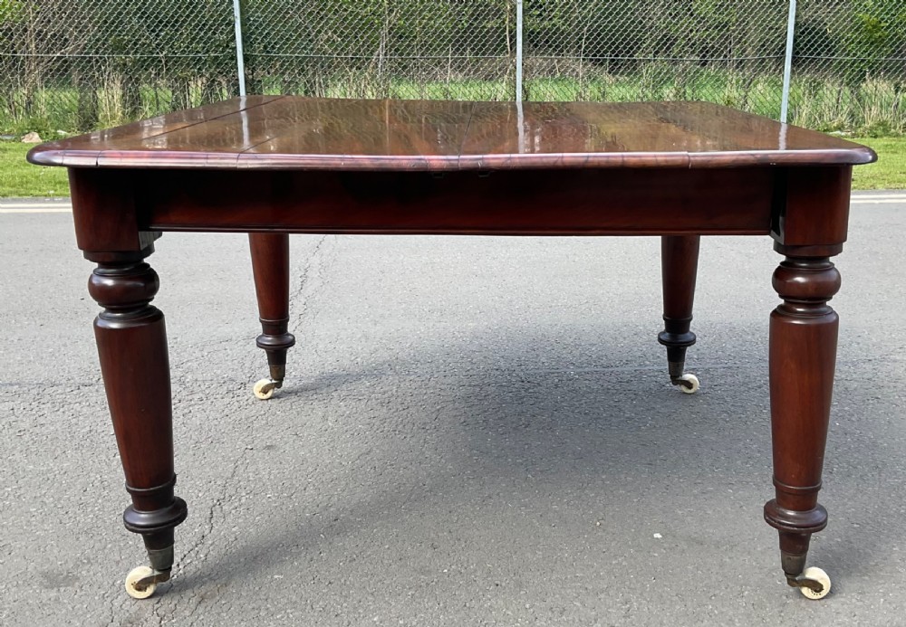 A large William IV mahogany extending dining table with turned tapered legs resting on brass and ceramic castors. View X